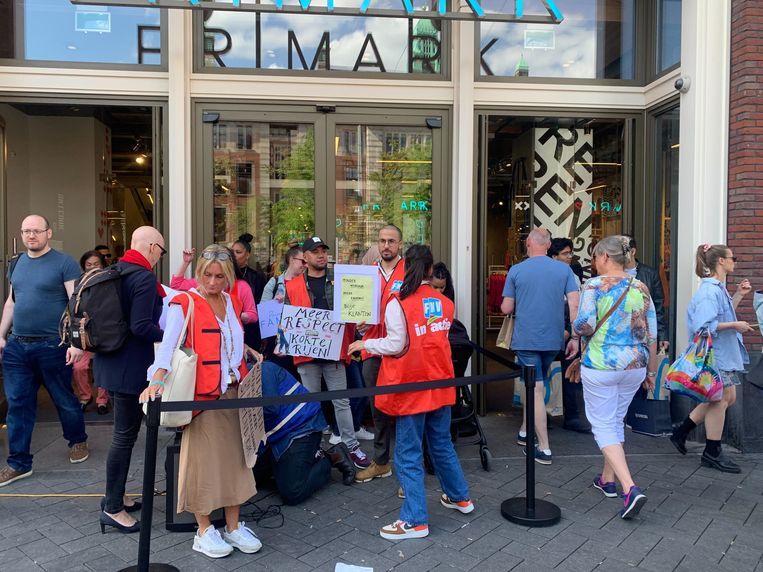 Protesters wearing FNV jackets gather in front of Primark in Amsterdam.  Statue of Anna Livia de Corte